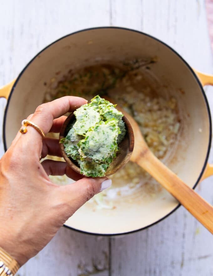 A hand holding the basil pesto in a bowl ready to add to the soup