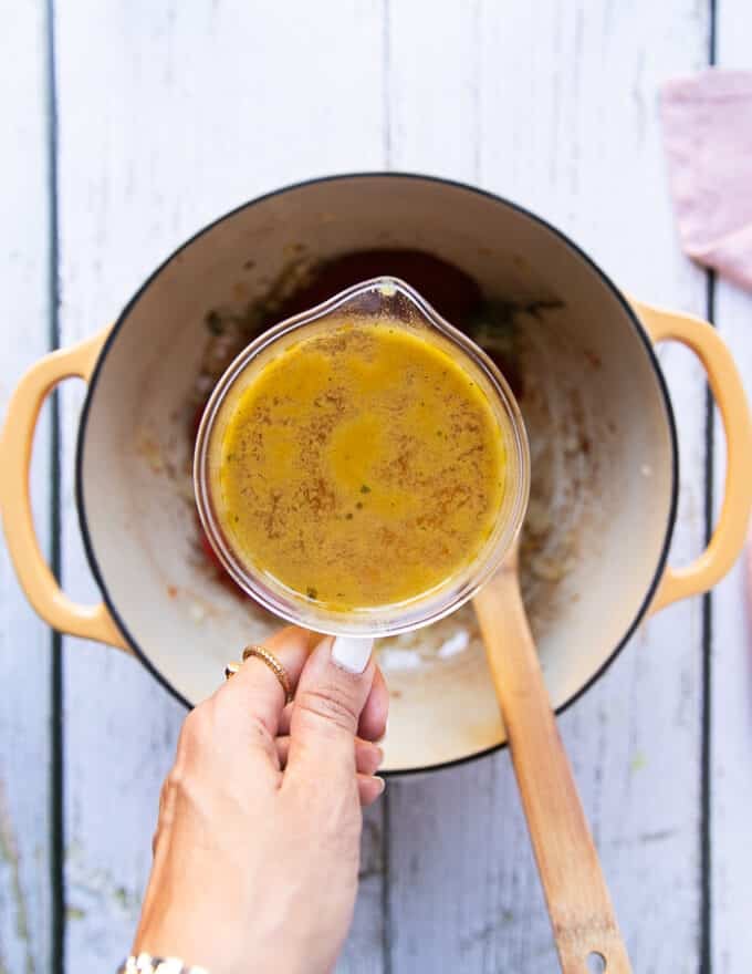 A hand holding the stock in a bowl ready to add to the soup