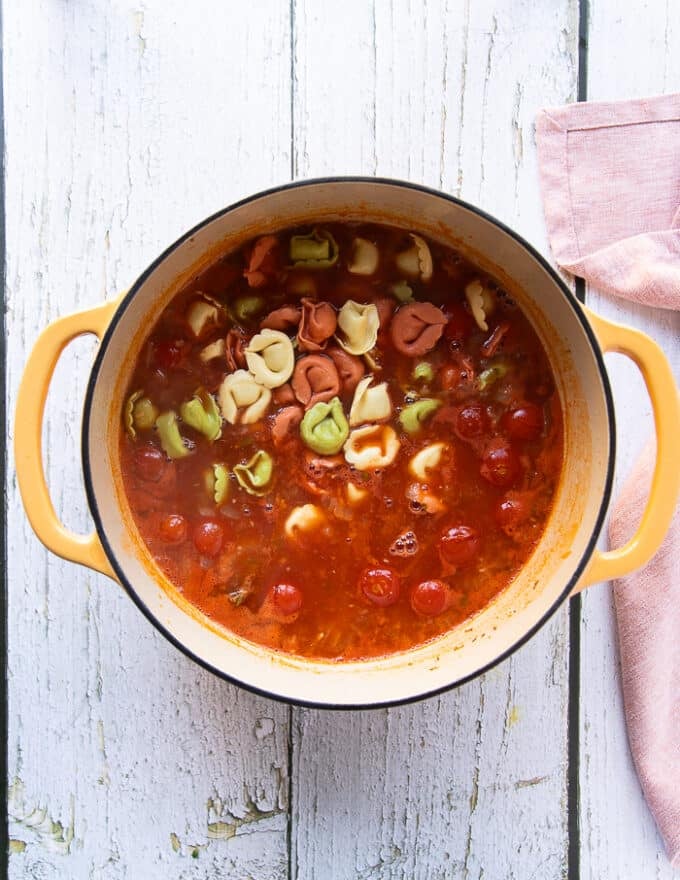 The tortellini is added to the pot of simmering tomato broth to cook