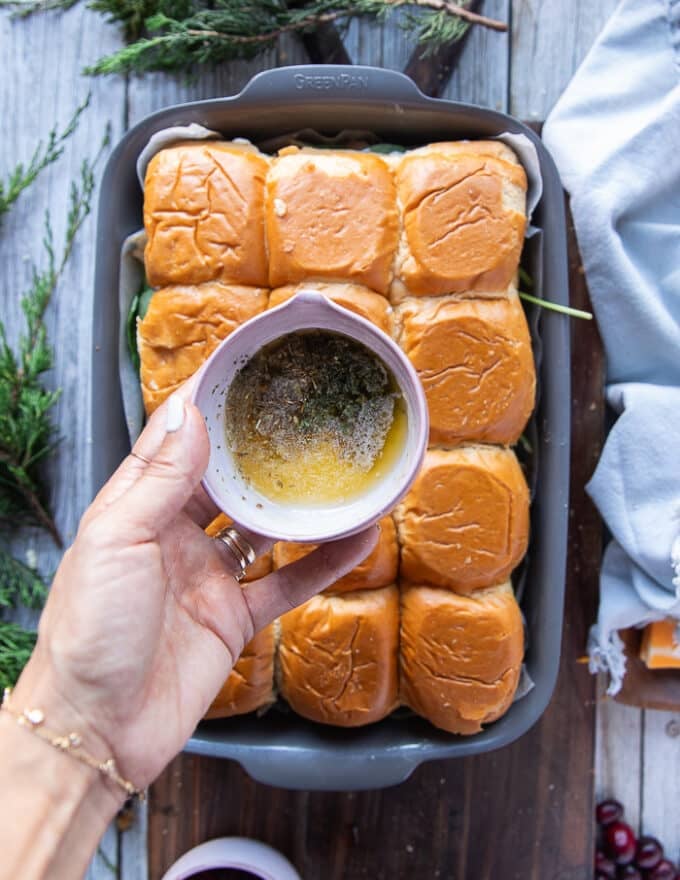 A hand holding a bowl of melted butter adding to it garlic powder, salt and dried oregano 