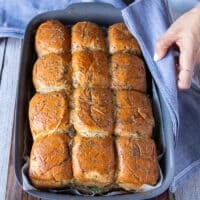 Turkey sliders out of the oven in the pan and a hand holding a kitchen towel to show them