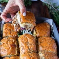 A hand pulling out one turkey slider from the pan showing a cheese stretch and the filling of turkey and cheese