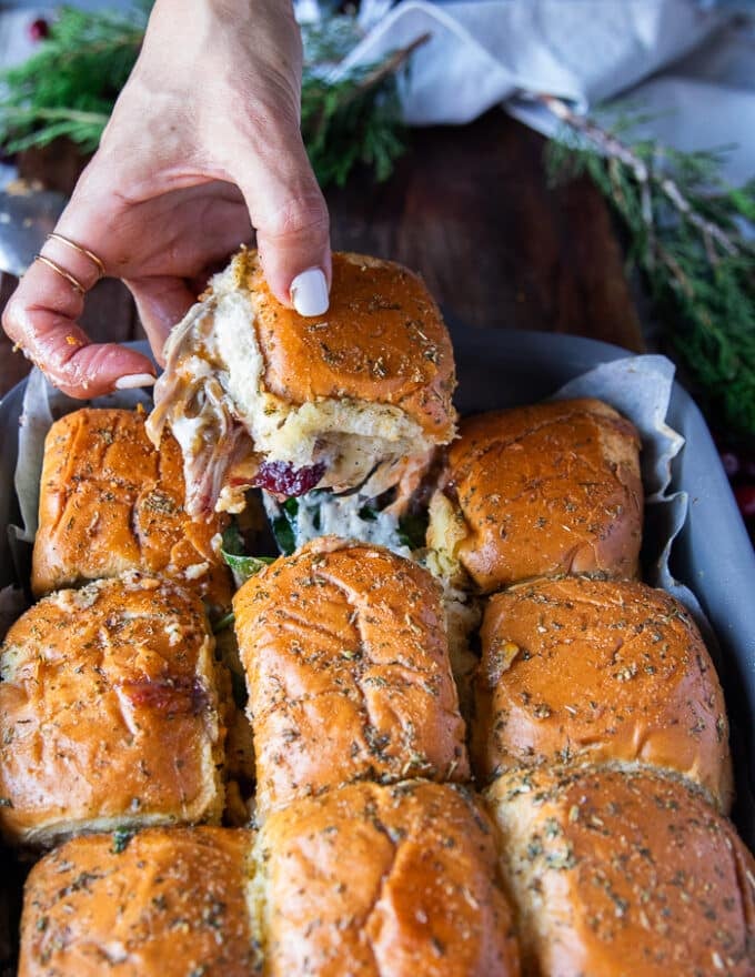 A hand pulling out one turkey slider from the pan showing a cheese stretch and the filling of turkey and cheese