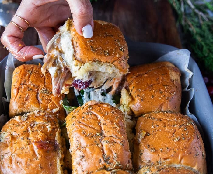 A hand pulling out one turkey slider from the pan showing a cheese stretch and the filling of turkey and cheese