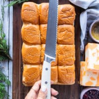 A hand holding a serrated knife to cut cross sectionally the hawaiian rolls bread or slider bread.