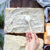 A hand spreading a generous amount of the garlic parmesan sauce at the bottom and top halves of the bread