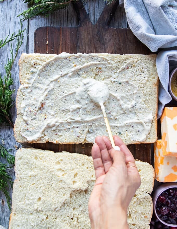 A hand spreading a generous amount of the garlic parmesan sauce at the bottom and top halves of the bread