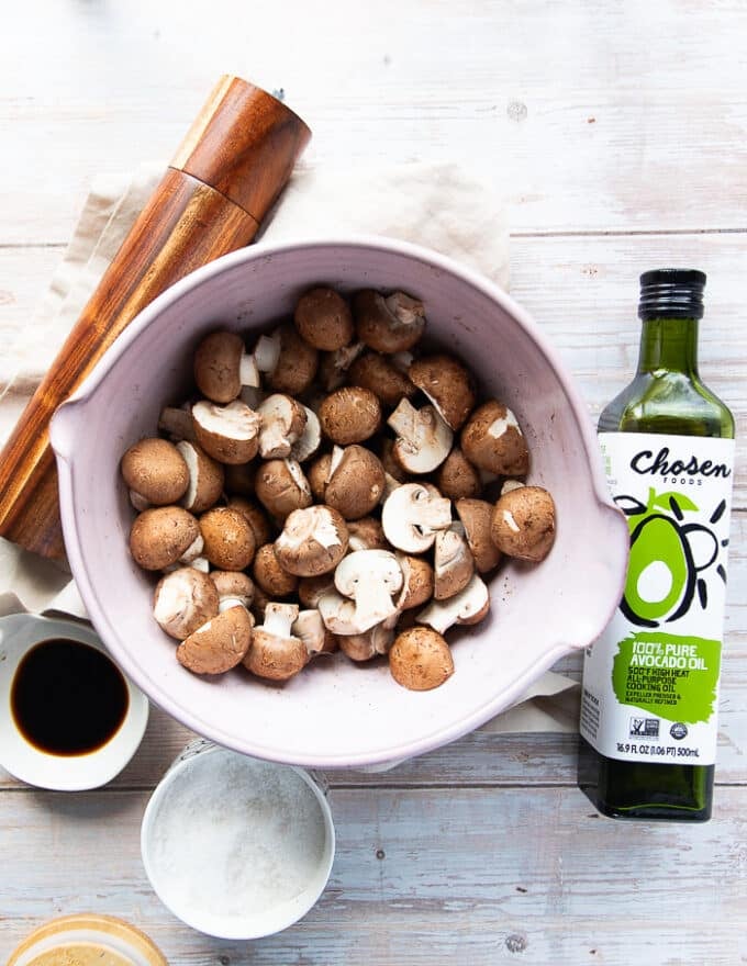 air fryer mushroom ingredients on a board which includes a bowl of mushrooms, a bottle of oil, some salt, pepper and soy sauce