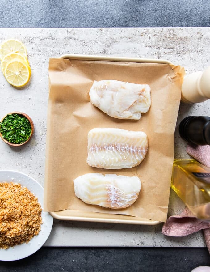 Ingredients for the baked cod including fresh cod fish, some panko bread crumbs, garlic, salt and pepper, olive oil, mustard, fresh herbs and lemon