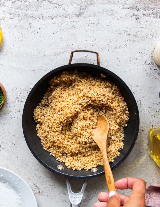 The crispy bread crumb coating is toasted and golden in the skillet with a hand tossing it, and ready to cool down