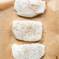 cod fillets on a baking sheet lined with parchment paper seasoned on both sides with salt and pepper