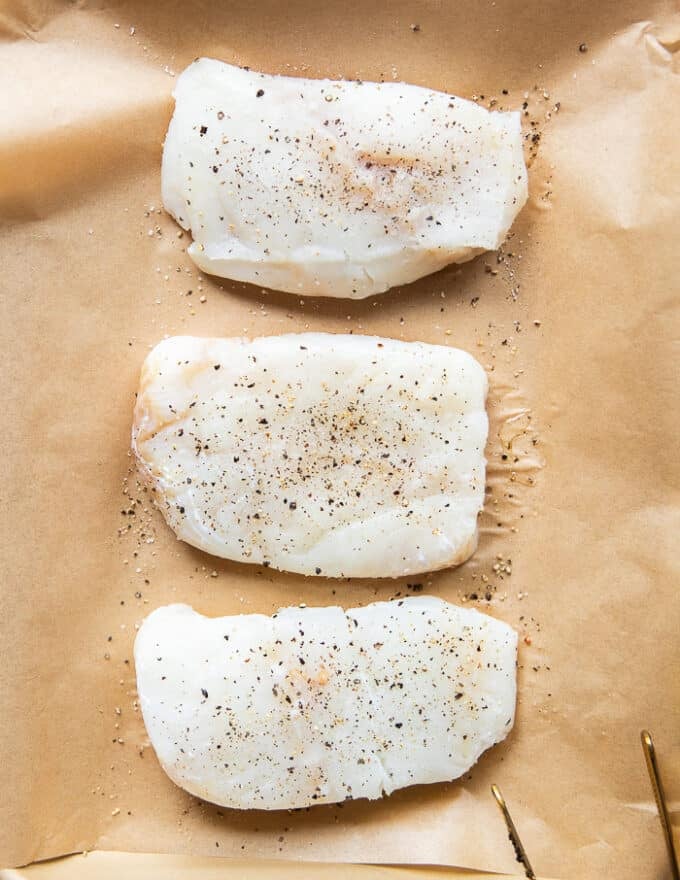 cod fillets on a baking sheet lined with parchment paper seasoned on both sides with salt and pepper 