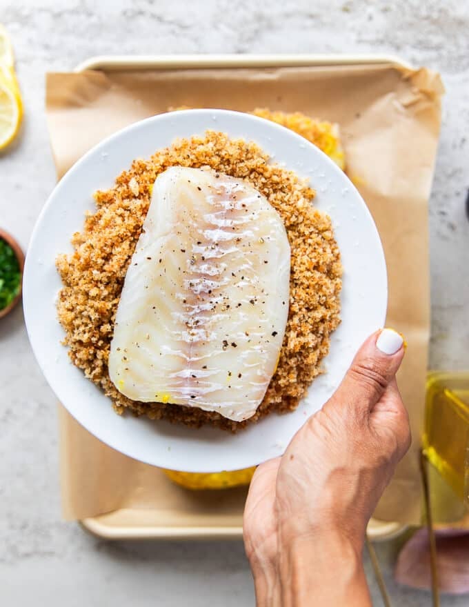 the mustard side of the fish dipped into the toasted bread crumbs and a hand pressing it down 