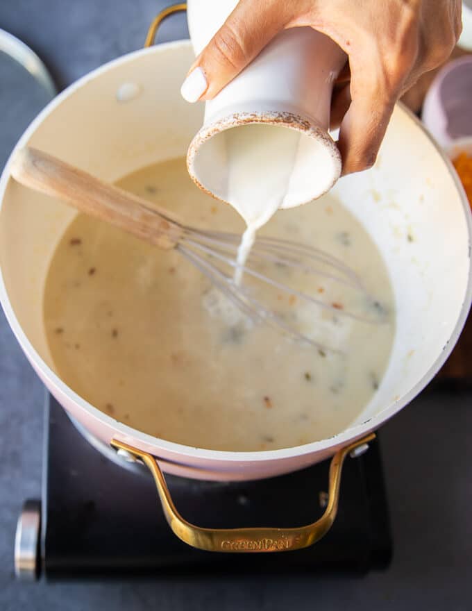 A hand now adding in a stream of milk into the soup