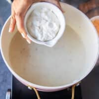 A hand adding in the sour cream into the baked potato soup