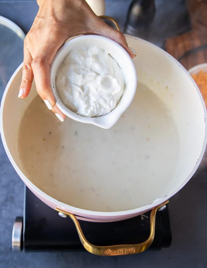 A hand adding in the sour cream into the baked potato soup 