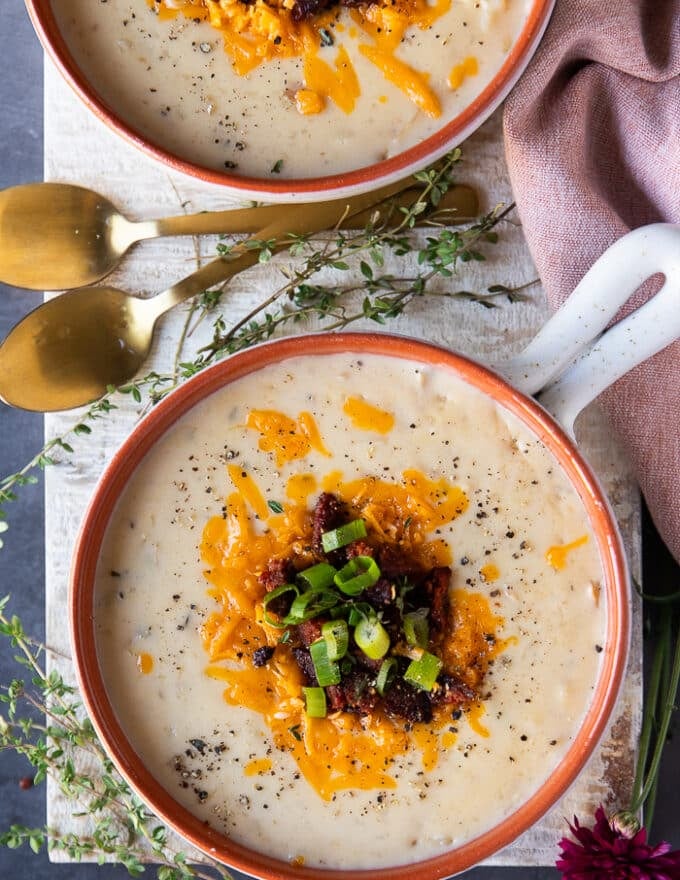 top view of one bowl of baked potato soup topped with crumbles, cheddar cheese, green onions and some cracked black pepper