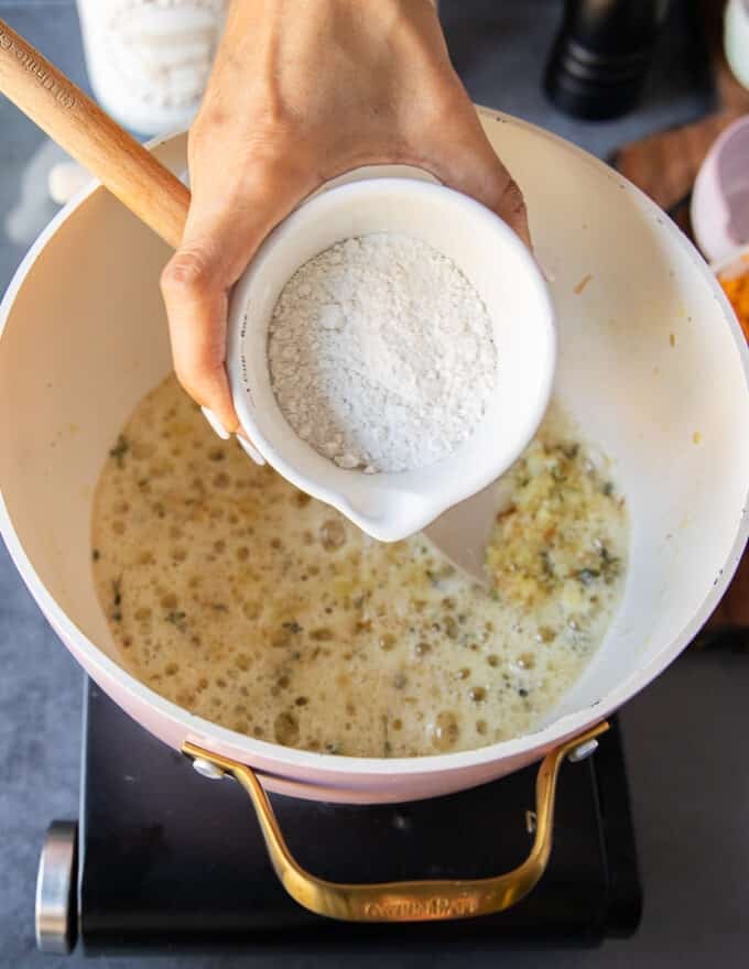 A hand adding in the flour into the onion and butter soup base in the pan