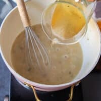 A stock is added gradually to the flour mixture and a hand holding a whisk is whisking it in gradually