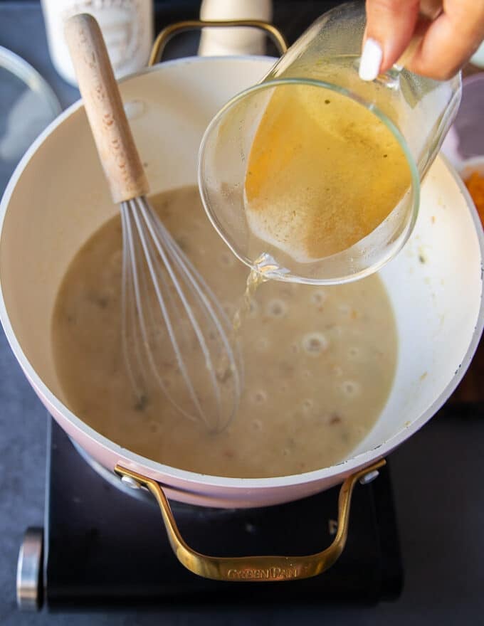 A stock is added gradually to the flour mixture and a hand holding a whisk is whisking it in gradually 
