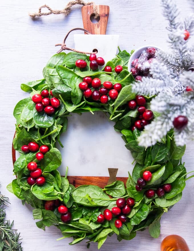 optional way of serving for the holidays-- a wreath made by fresh baby spinach leaves in a round shape, and then some fresh cranberries dotted aver the wreath to make it look super festive and placed over a round white marble