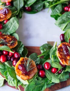 A close up of a cranberry and brie bite baked over puff pastry and garnished with cranberry sauce and rosemary, over a bed of spinach