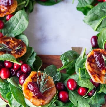 A close up of a cranberry and brie bite baked over puff pastry and garnished with cranberry sauce and rosemary, over a bed of spinach