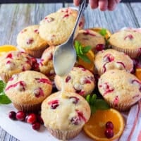 A hand holding a spoon and drizzling the glaze right over the muffins