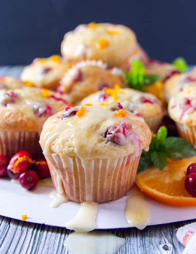 Close up of one cranberry orange muffin upright on a wooden board with the orange glaze dripping