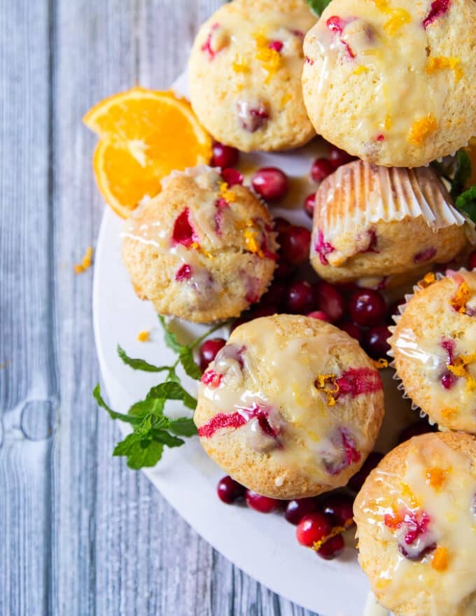 Close up top view of half the board of orange cranberry muffins focusing on one muffin very close showing the texture and glaze 