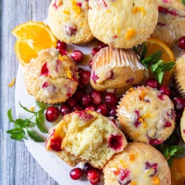 A board of cranberry orange muffins glazed and one of the muffins is cut into half to show closely the soft and fluffy texture of the muffins