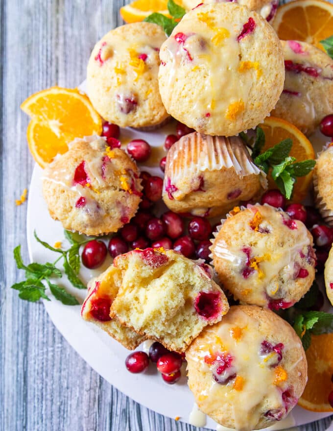 A board of cranberry orange muffins glazed and one of the muffins is cut into half to show closely the soft and fluffy texture of the muffins