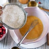 A hand pouring the dry ingredients into the large bowl of wet ingredients mixed in.