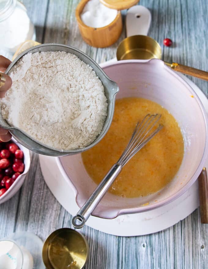 A hand pouring the dry ingredients into the large bowl of wet ingredients mixed in.