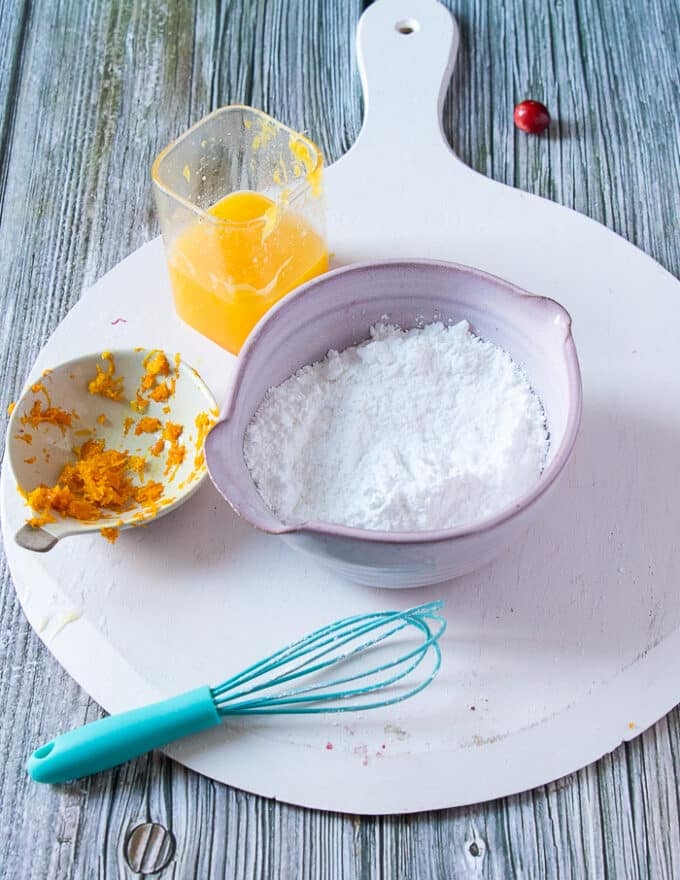 Ingredients for the orange glaze including a bowl of confectioner sugar, some orange juice and some orange zest in small bowls