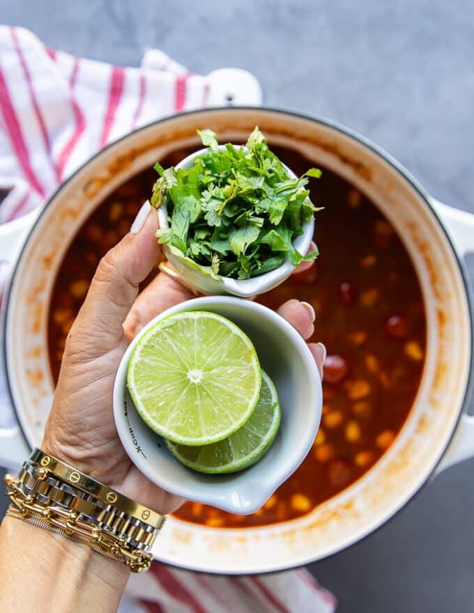 A hand holding a handful of cilantro and a lime cut in half ready to squeeze it in as the taco soup recipe is complete