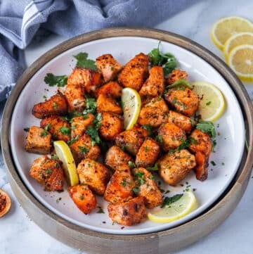 salmon bites on a plate with lime slices and fresh parsley surrounded by lemon slices
