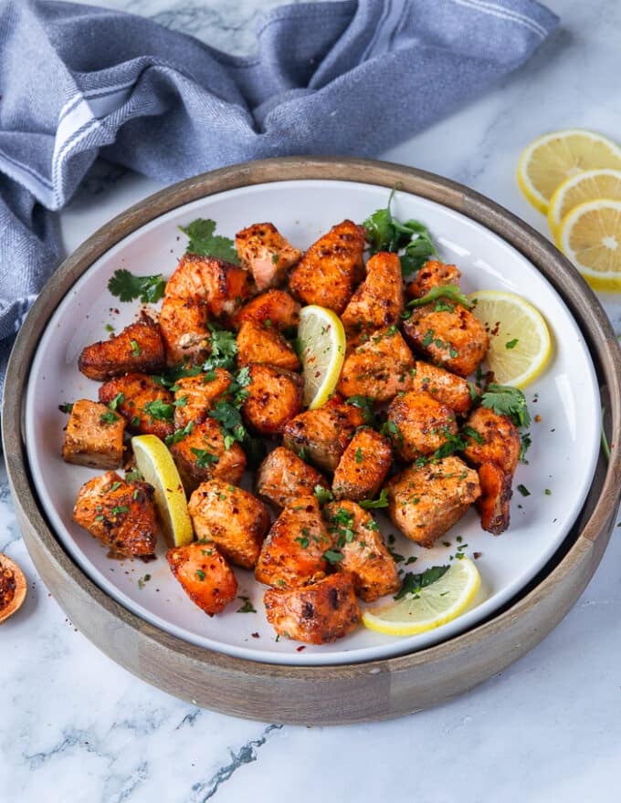 salmon bites on a plate with lime slices and fresh parsley surrounded by lemon slices