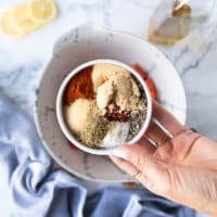 A hand holding the spice blend in a small plate ready to mix it and add it to the salmon bowl