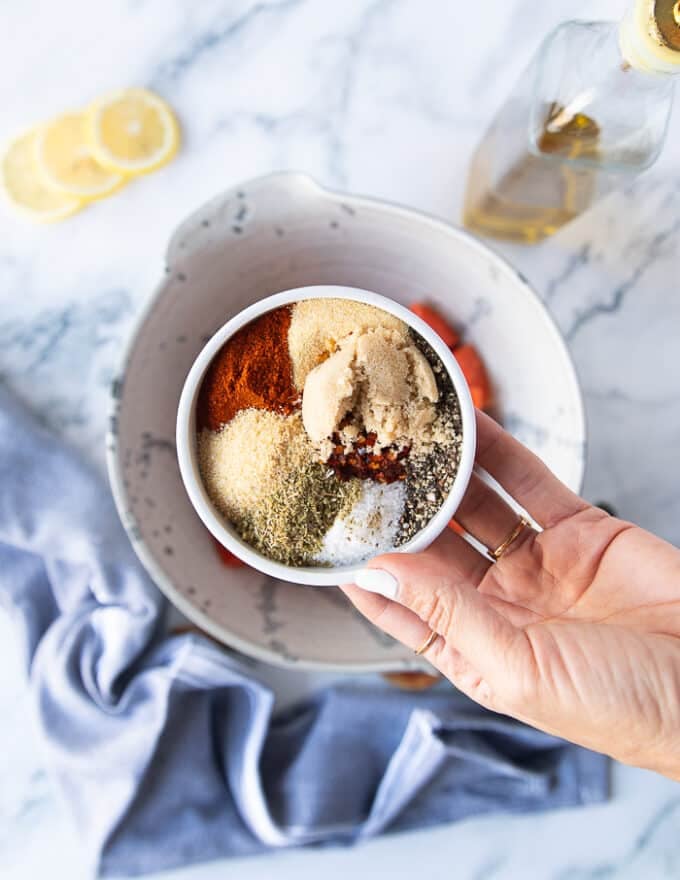 A hand holding the spice blend in a small plate ready to mix it and add it to the salmon bowl