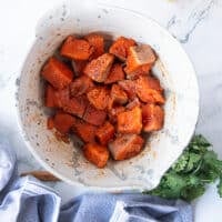 A bowl with 1 inch cut up salmon bites tossed in the spice mixture and olive oil and read to cook