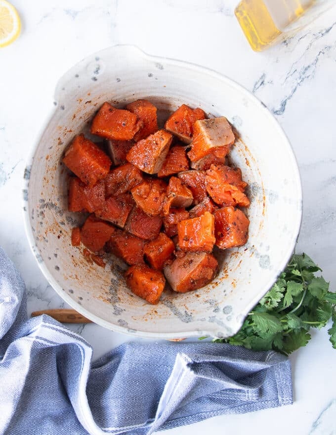 A bowl with 1 inch cut up salmon bites tossed in the spice mixture and olive oil and read to cook