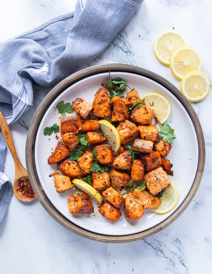 Salmon bites cooked on a plate garnished with cilantro and lemon