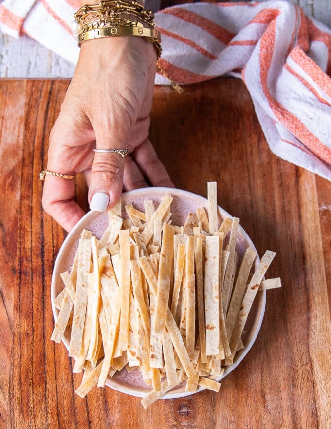 A hand holding a plate of tortillas cut into thin strips