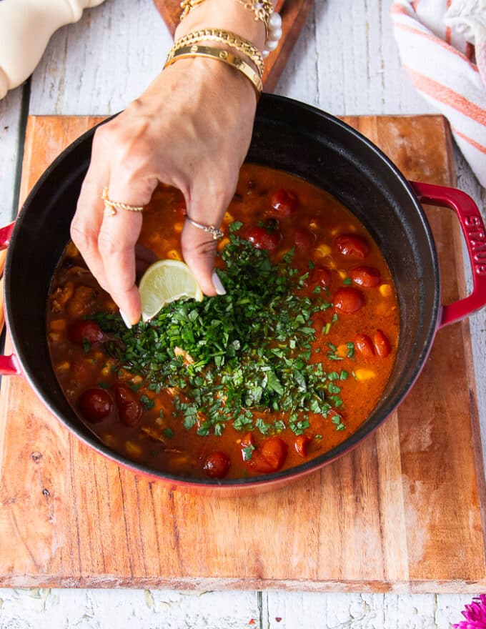 chicken tortilla soup is ready and a hand is squeezing lime over it in the pot and a added cilantro