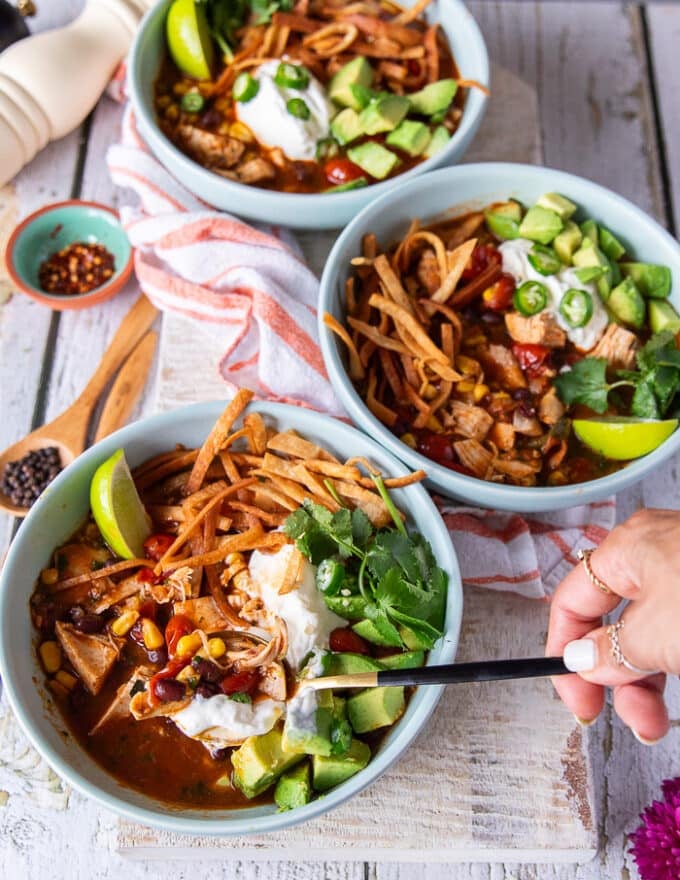 A hand holding a spoon and spooning out some chicken tortilla soup from a bowl