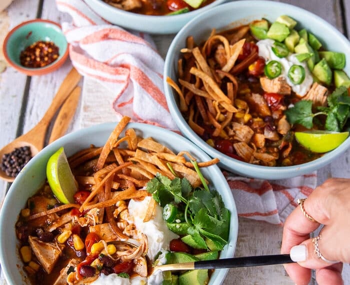 A hand holding a spoon and spooning out some chicken tortilla soup from a bowl