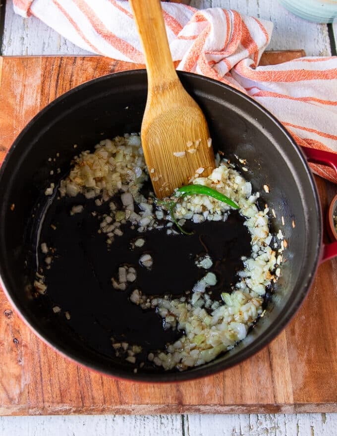 One large pot with onions and jalapeños sautéing and a wooden spoon mixing it in