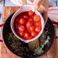 A hand adding the canned tomatoes in juices right into the pot