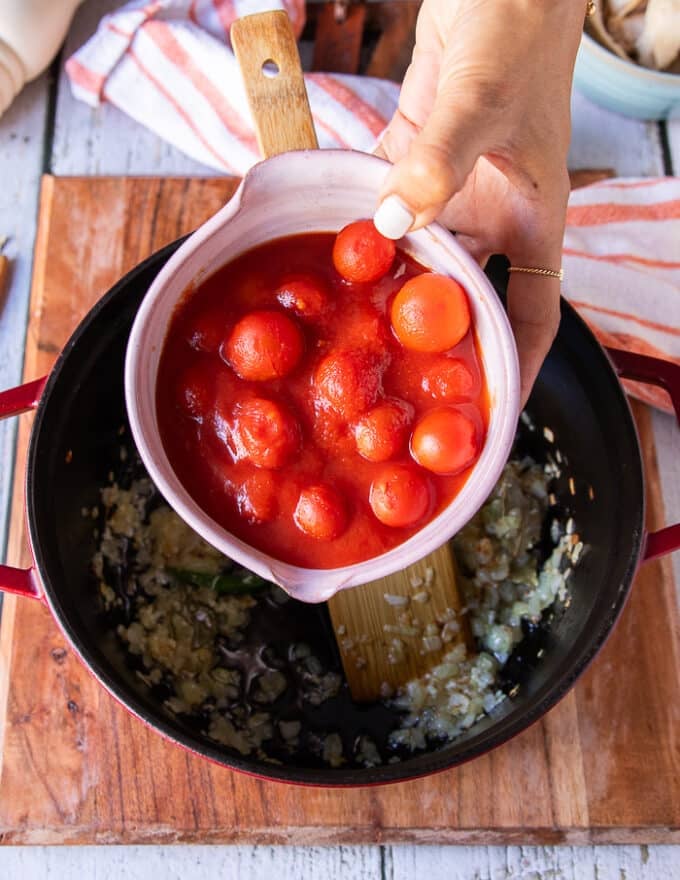 A hand adding the canned tomatoes in juices right into the pot